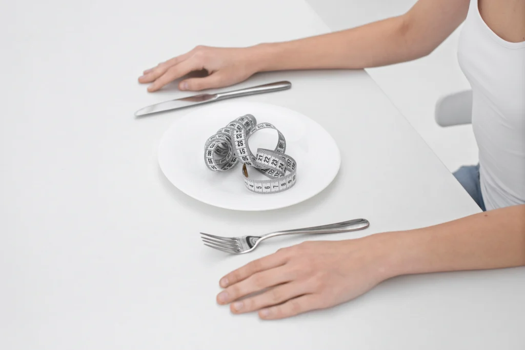 Cinta métrica enrollada en un plato vacío con cuchillo y tenedor