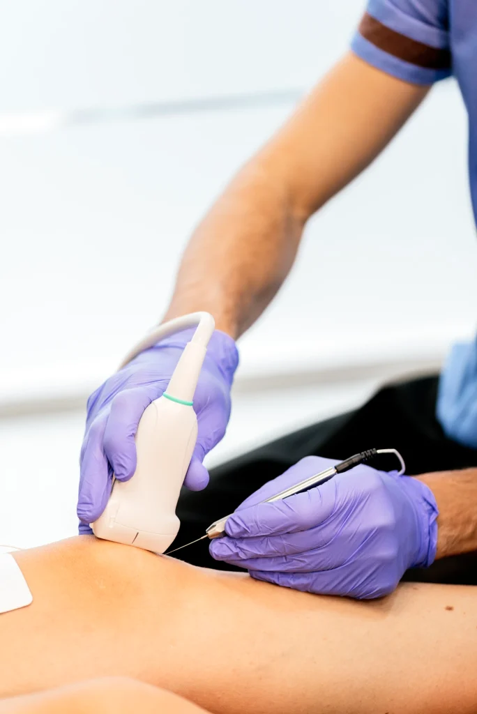 Fisioterapeuta con guantes aplicando una punción guiada con ecógrafo en la espalda de un paciente