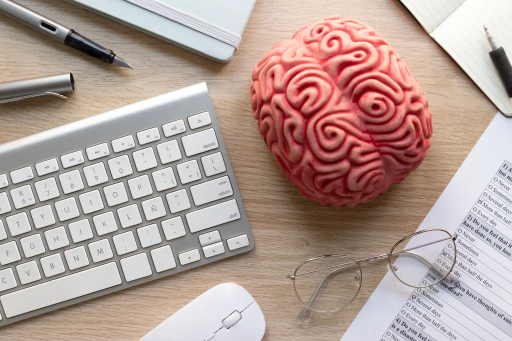 Modelo de cerebro junto a un teclado y unas gafas sobre una mesa de trabajo